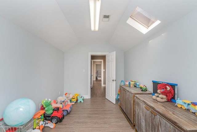 playroom with lofted ceiling with skylight, visible vents, and light wood finished floors