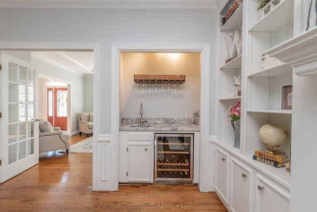 bar featuring light wood-type flooring, a sink, wine cooler, crown molding, and wet bar