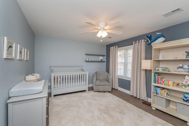 bedroom featuring visible vents, wood finished floors, a nursery area, baseboards, and ceiling fan