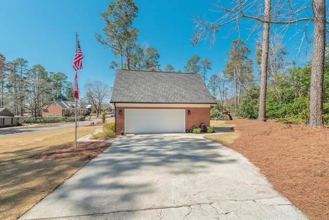 view of front facade with a front lawn, roof with shingles, concrete driveway, an attached garage, and brick siding