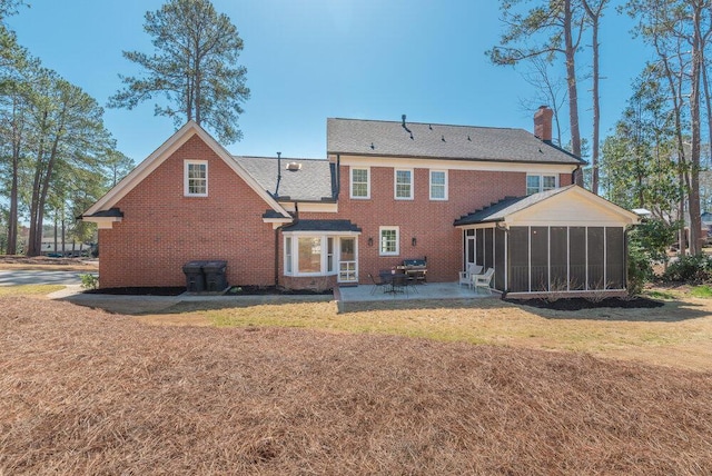 back of house featuring a yard, a sunroom, a chimney, a patio area, and brick siding