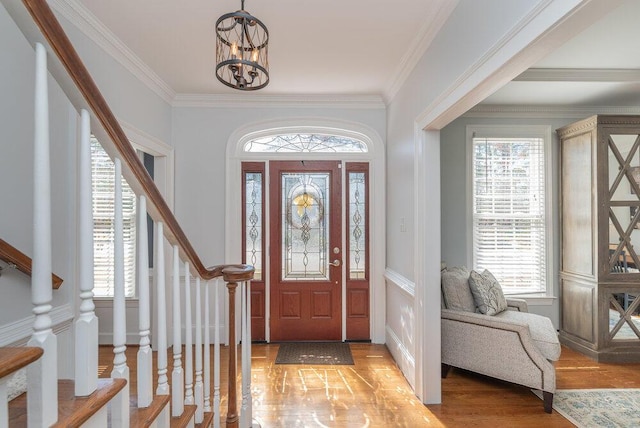 foyer with stairs, an inviting chandelier, light wood-style floors, and ornamental molding