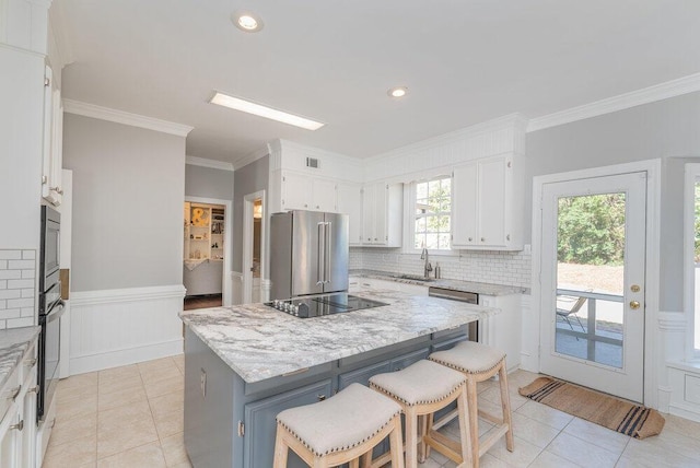 kitchen with white cabinetry, black appliances, wainscoting, and a sink