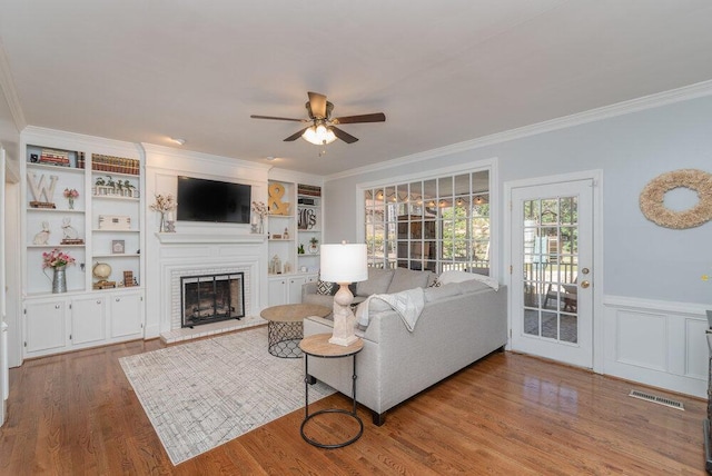 living room with wood finished floors, ceiling fan, a fireplace, and crown molding