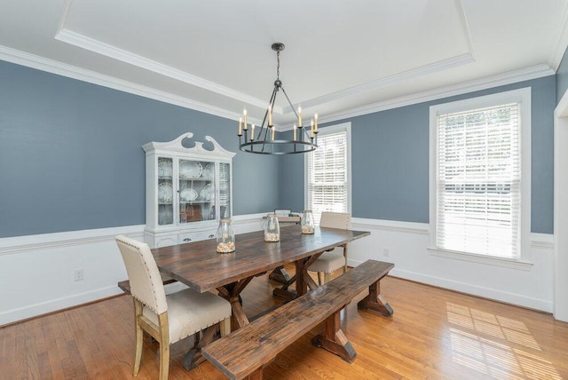 dining area featuring wood finished floors, a tray ceiling, wainscoting, crown molding, and a chandelier