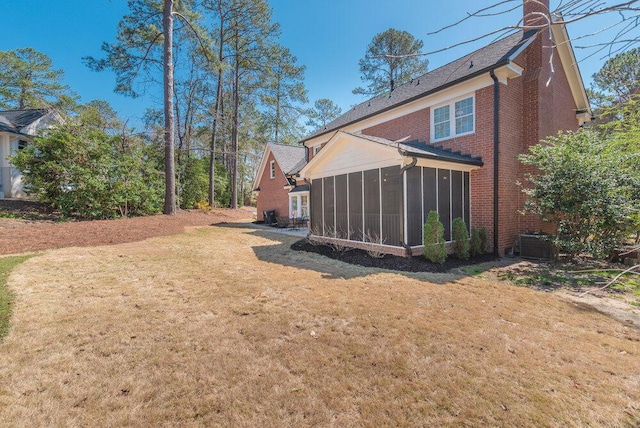 back of house with a yard, roof with shingles, a sunroom, brick siding, and a chimney