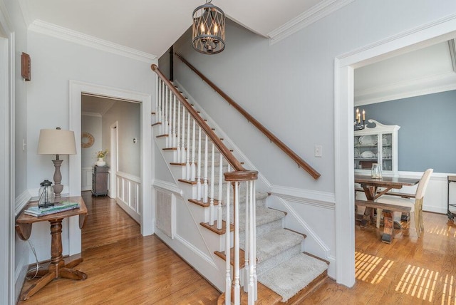 stairs featuring an inviting chandelier, crown molding, and wood finished floors