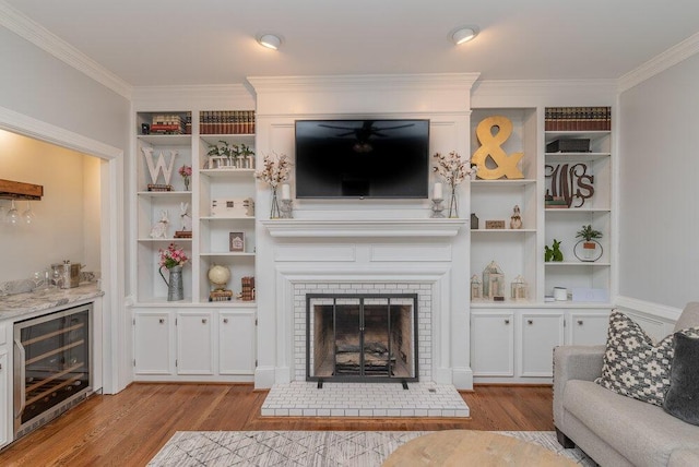 living area with wood finished floors, wine cooler, a fireplace, crown molding, and ceiling fan