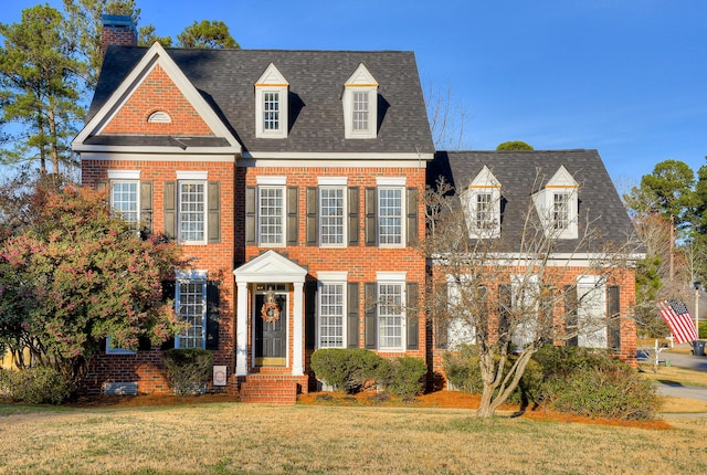 colonial house featuring brick siding, a front lawn, and roof with shingles