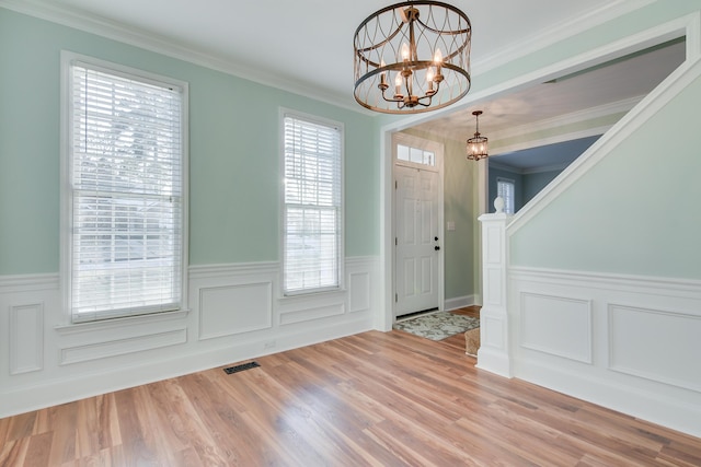 entrance foyer featuring a notable chandelier, visible vents, ornamental molding, wainscoting, and wood finished floors