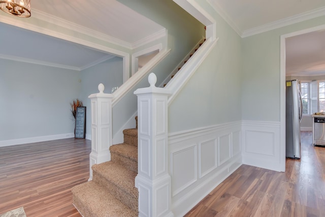 staircase featuring ornamental molding, wainscoting, wood finished floors, and a decorative wall