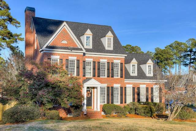 colonial-style house featuring a shingled roof, a front lawn, and brick siding