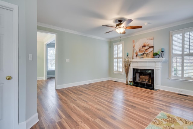 unfurnished living room featuring plenty of natural light, ornamental molding, a fireplace, and wood finished floors