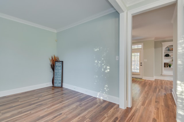 spare room featuring baseboards, wood finished floors, and crown molding