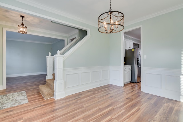 unfurnished room with ornamental molding, light wood-type flooring, stairway, and an inviting chandelier