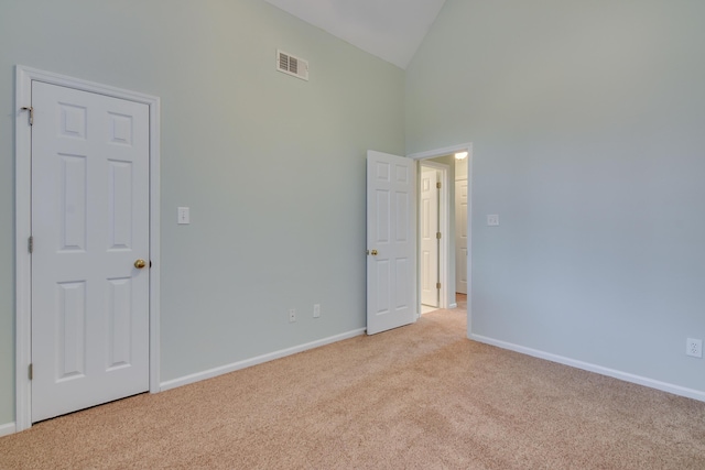 empty room featuring high vaulted ceiling, carpet, visible vents, and baseboards