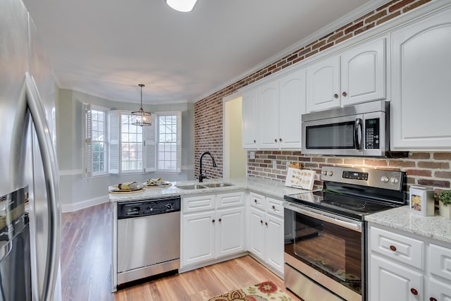 kitchen featuring light wood-style flooring, a peninsula, a sink, ornamental molding, and appliances with stainless steel finishes