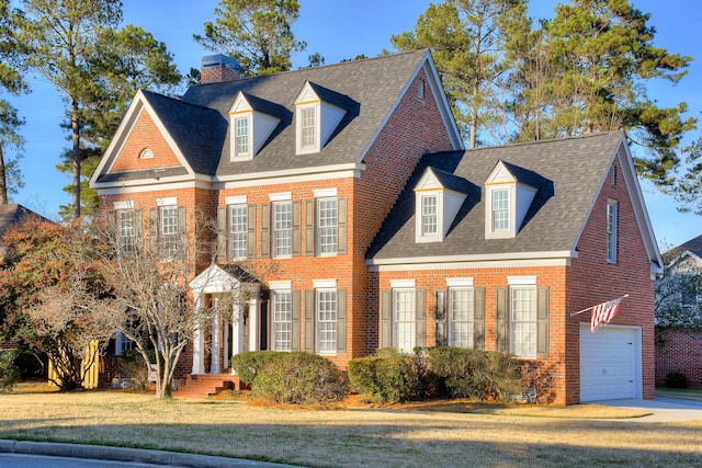 georgian-style home featuring driveway, brick siding, a shingled roof, an attached garage, and a front yard