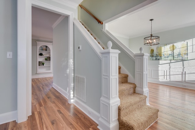 staircase featuring a chandelier, ornamental molding, wood finished floors, and visible vents