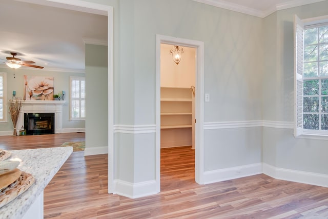 spare room with ornamental molding, a glass covered fireplace, a wealth of natural light, and light wood-type flooring