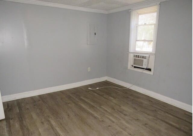 unfurnished room with electric panel, dark hardwood / wood-style floors, cooling unit, and crown molding