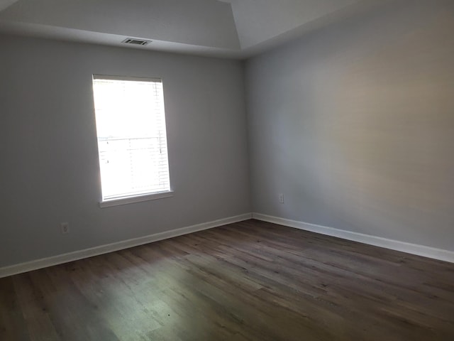 empty room with lofted ceiling, dark wood-type flooring, visible vents, and baseboards
