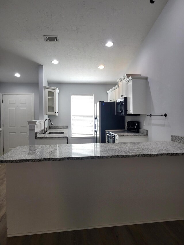 kitchen featuring a sink, range with electric cooktop, stainless steel fridge, black microwave, and visible vents