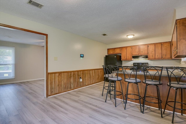 kitchen featuring black refrigerator, a breakfast bar, a textured ceiling, electric stove, and light hardwood / wood-style flooring