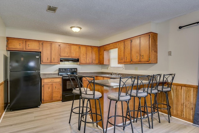 kitchen with black appliances, kitchen peninsula, a textured ceiling, and wooden walls