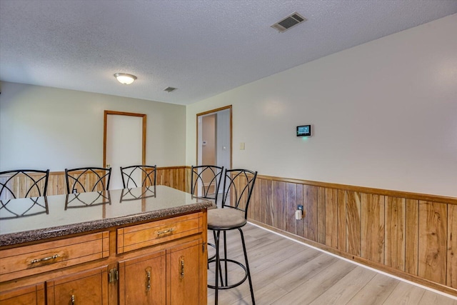 kitchen with light wood-type flooring, a textured ceiling, a breakfast bar area, and wood walls