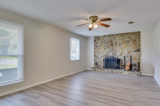 unfurnished living room with ceiling fan, light hardwood / wood-style floors, and a stone fireplace