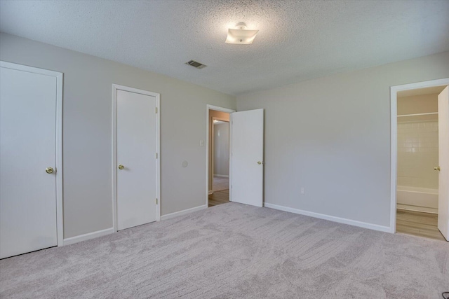 unfurnished bedroom featuring a textured ceiling, light carpet, and connected bathroom