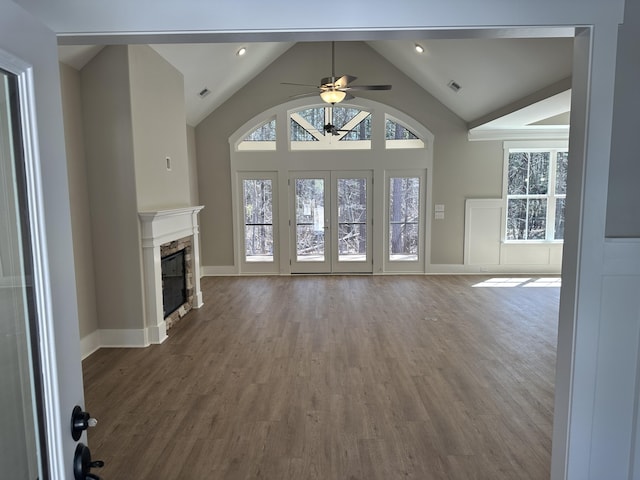 unfurnished living room featuring a stone fireplace, a healthy amount of sunlight, and wood finished floors