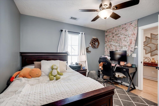 bedroom with baseboards, visible vents, a ceiling fan, wood finished floors, and a textured ceiling