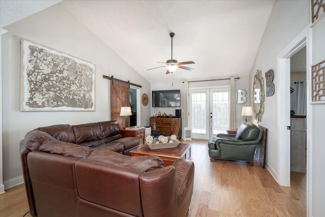 living area featuring lofted ceiling, ceiling fan, a barn door, light wood-style floors, and french doors