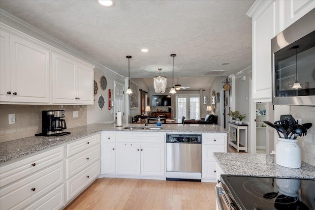 kitchen with open floor plan, a peninsula, stainless steel appliances, light wood-style floors, and a sink