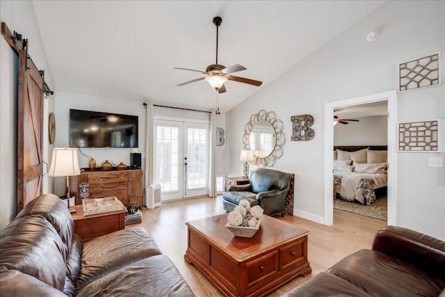 living room with lofted ceiling, a barn door, a ceiling fan, light wood-style floors, and french doors