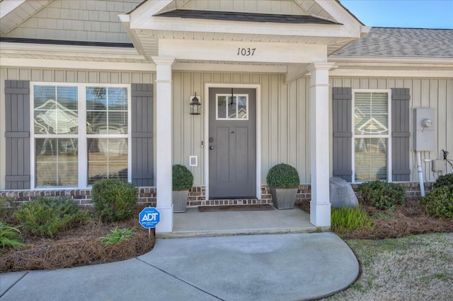 doorway to property with a porch, roof with shingles, and board and batten siding