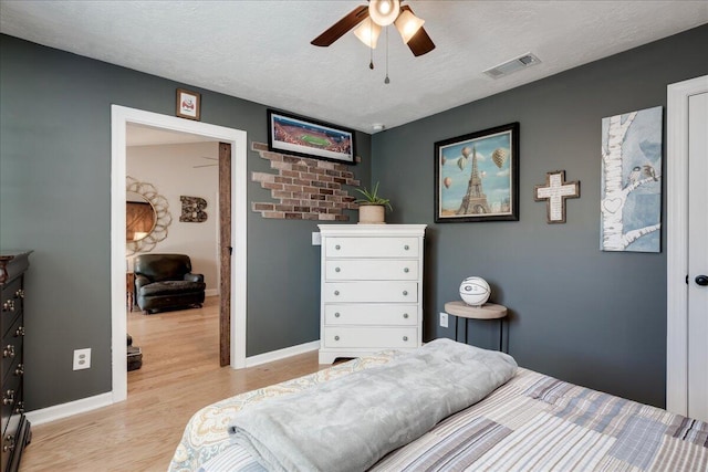 bedroom with baseboards, visible vents, a ceiling fan, a textured ceiling, and light wood-type flooring