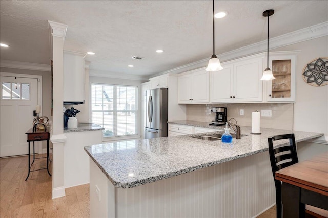 kitchen featuring a peninsula, a sink, ornamental molding, light wood-type flooring, and freestanding refrigerator