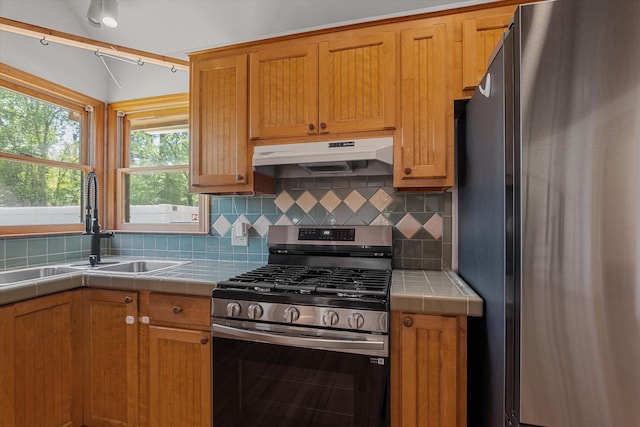 kitchen with stainless steel appliances, a sink, backsplash, under cabinet range hood, and tile countertops