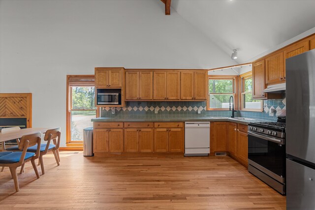 kitchen featuring high vaulted ceiling, a sink, under cabinet range hood, decorative backsplash, and appliances with stainless steel finishes