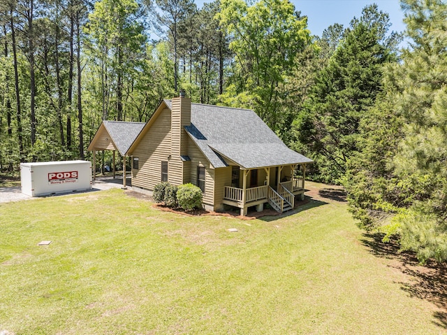 view of side of property featuring a lawn, a chimney, covered porch, and roof with shingles