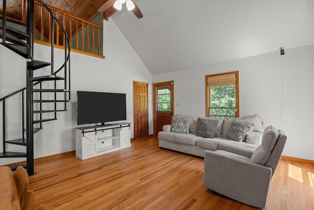 living room with baseboards, light wood-style floors, a ceiling fan, stairs, and high vaulted ceiling