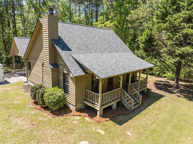 view of front of home with a shingled roof, covered porch, and a front yard