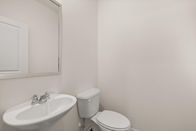 half bathroom with toilet, baseboards, and a sink