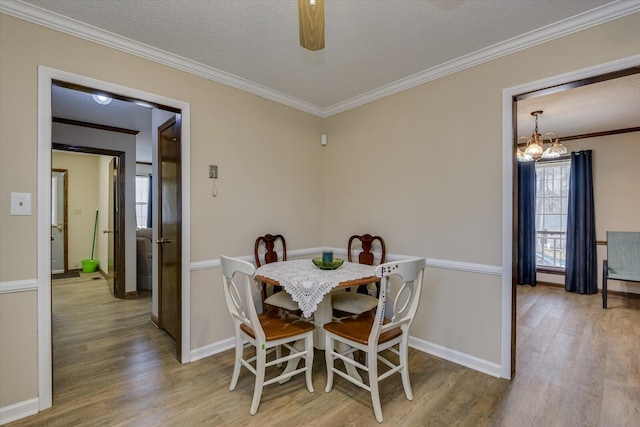 dining room featuring light wood-type flooring, crown molding, a textured ceiling, and ceiling fan with notable chandelier