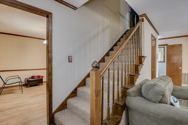 staircase with crown molding, a textured ceiling, and hardwood / wood-style floors