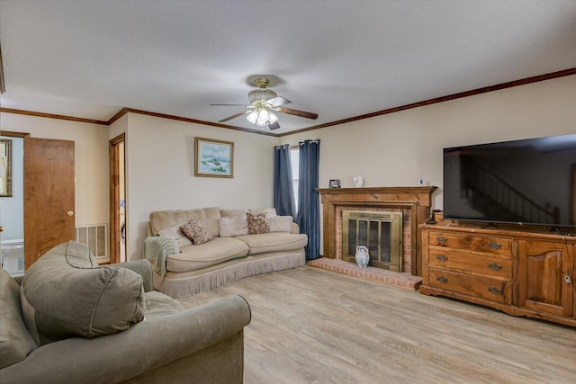 living room with a fireplace, light hardwood / wood-style flooring, ceiling fan, a textured ceiling, and crown molding