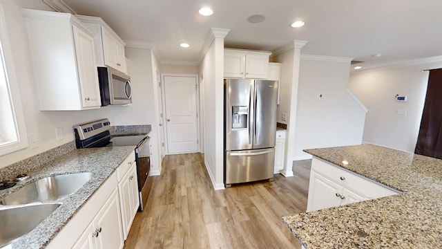 kitchen with white cabinets, appliances with stainless steel finishes, light stone countertops, and ornamental molding